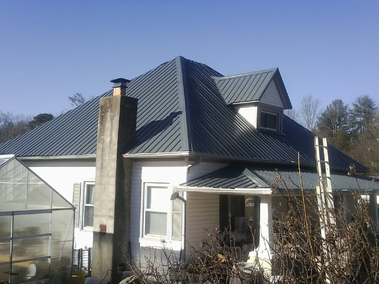 Dark blue standing seam metal roof on a white farmhouse with dormer — Slate & Tile Roof Repair by Roofing Brothers in Commerce City