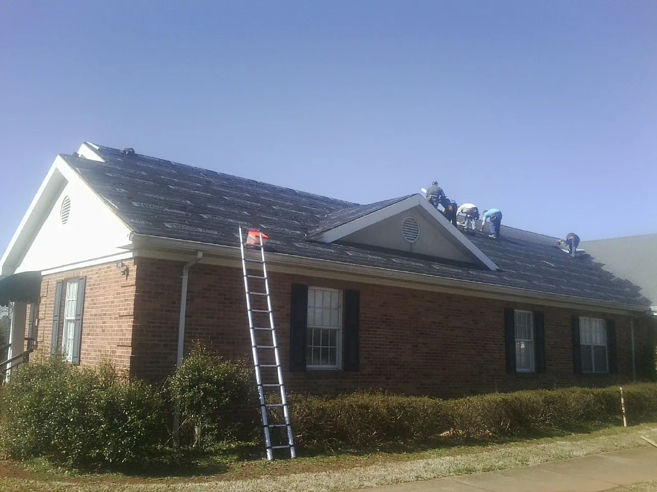 Crew tearing shingles off a brick ranch roof with a ladder set — Emergency Roof Repair work by our crew in Commerce City