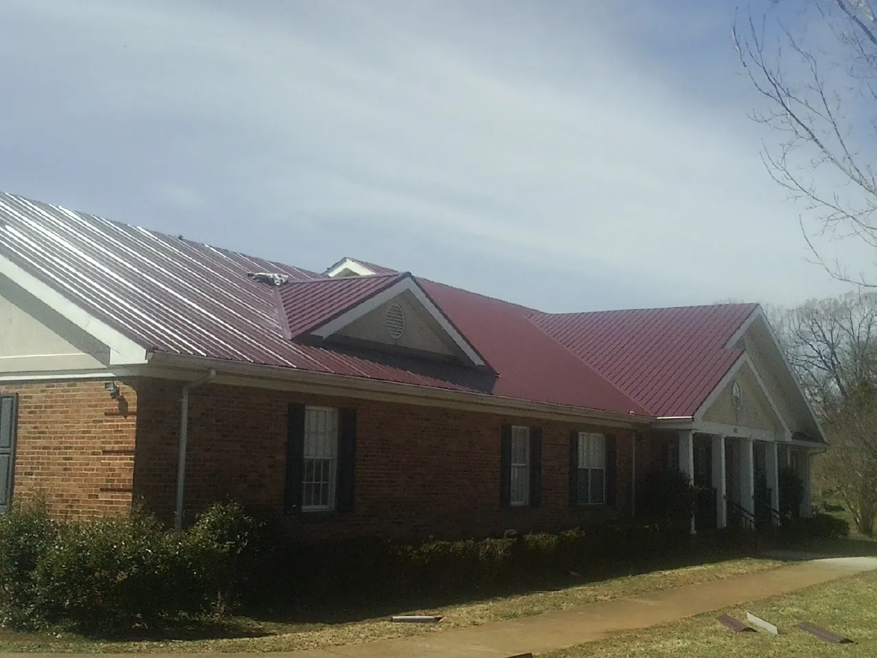 Red metal roof with gabled entries on a long brick building, from a Hail Damage Roof Repair job in Commerce City