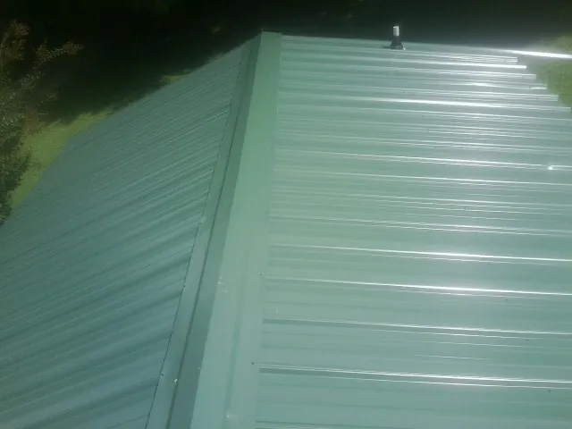 New green metal panels meeting at the ridge of a roof — Flat Roof Repair work by our crew in Commerce City