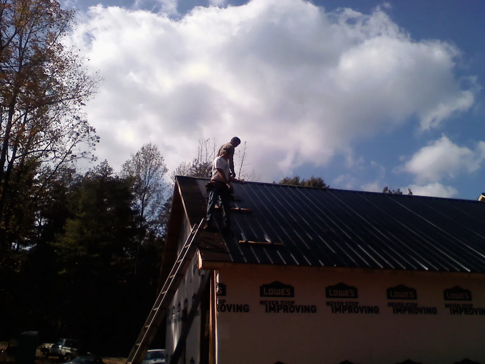 Roofer fastening dark metal panels high against a cloudy sky in Commerce City