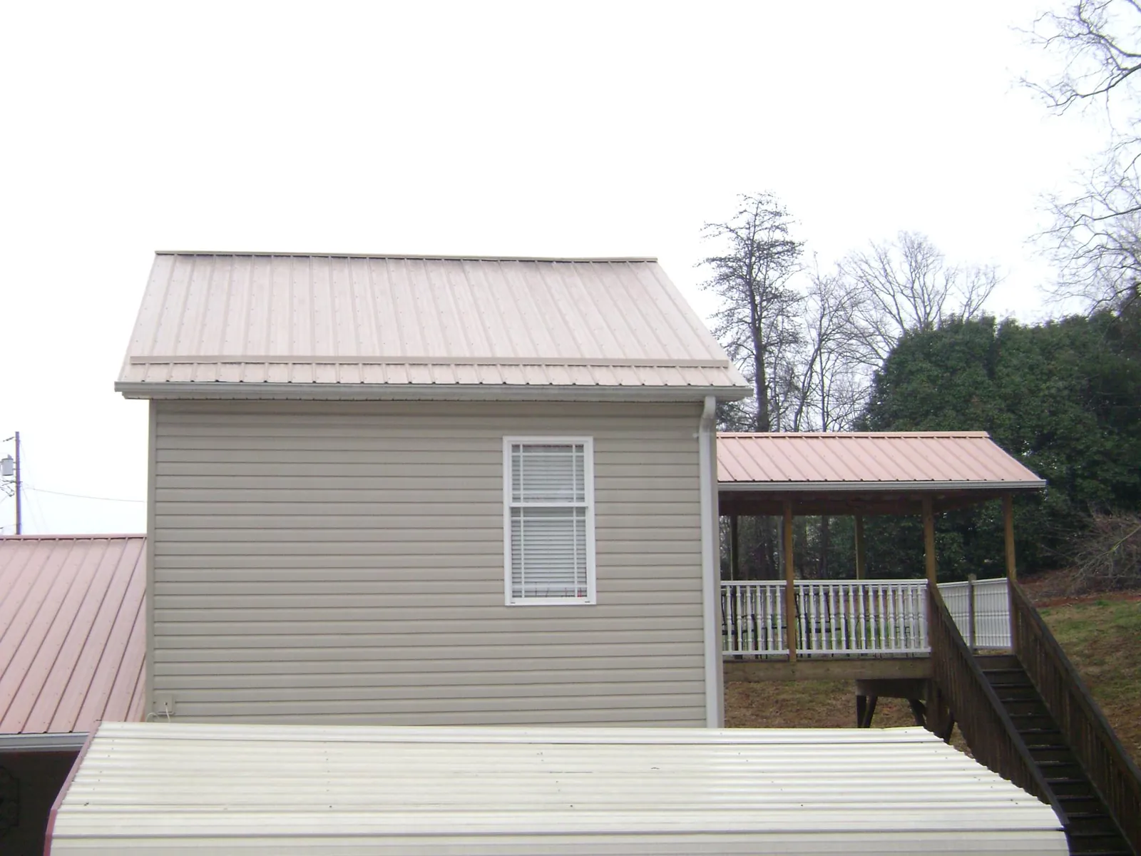 Tan metal roofs on a two story addition and attached porch, from a Roof Replacement job in Commerce City